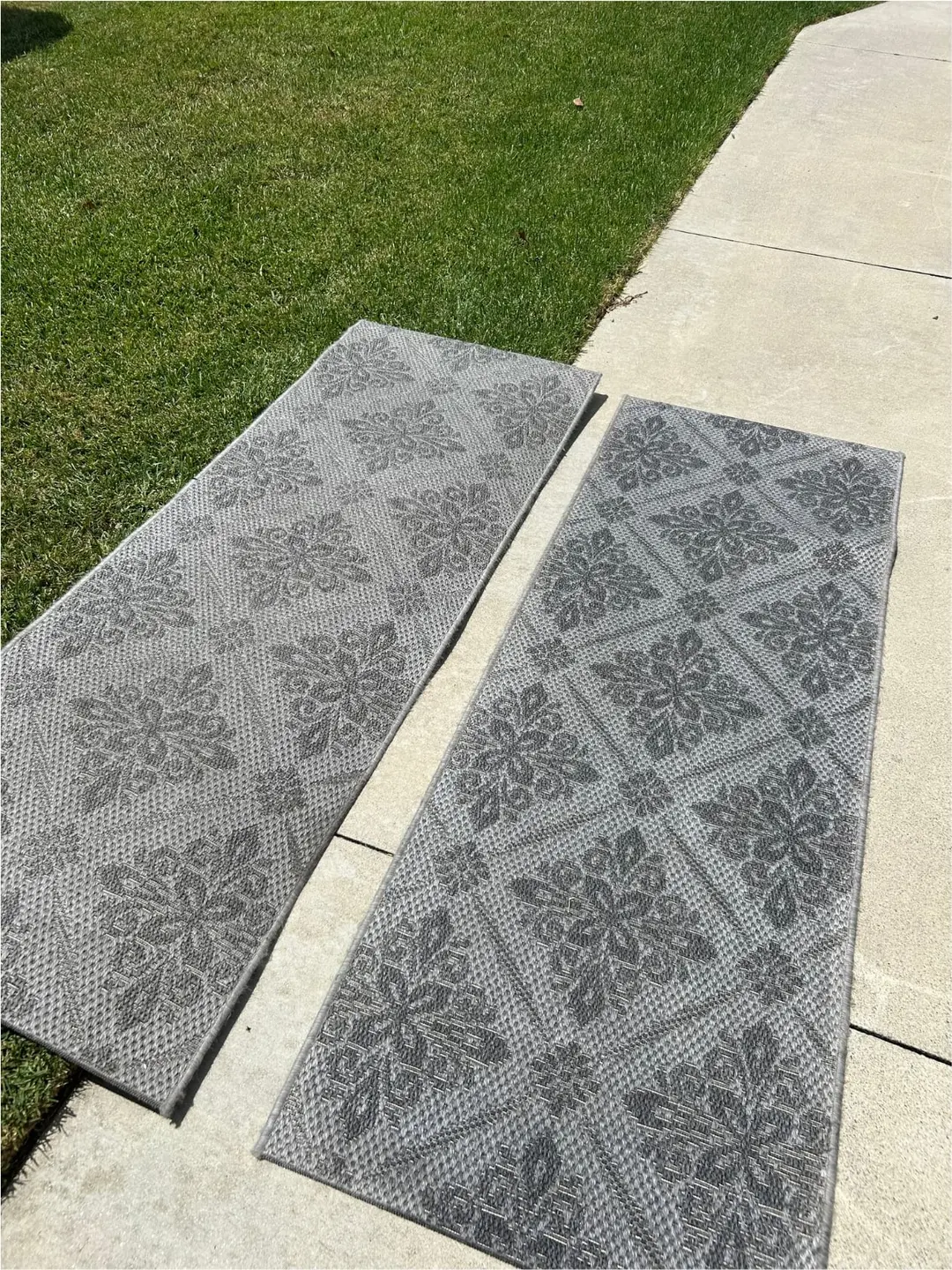 Two gray patterned rugs laid out beside a lawn on a concrete walkway